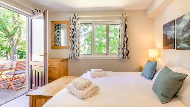 A bedroom with a bed, a nightstand, a lamp, a window with curtains, a dresser, and a mirror.