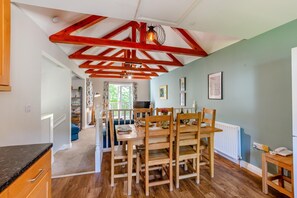 A dining area with wooden chairs and a table, a kitchen with a white countertop, and a ceiling with exposed beams.