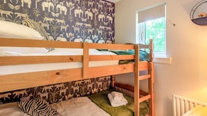 A bunk bed room with a jungle-themed wallpaper, a window with a view of greenery, and a radiator.