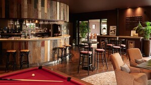 A bar area with stools, a pool table, and a bar counter with bottles.