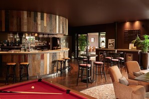 A bar area with stools, a pool table, and a bar counter with bottles.