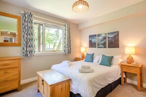 A bedroom with a bed, bedside tables, a wooden bench, a mirror, and a window with curtains.
