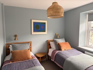 Ein Schlafzimmer mit zwei Betten, einem kleinen Tisch, einer Hängeleuchte und einem gerahmten Kunstwerk an der Wand.