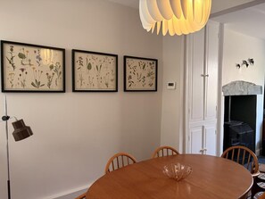 Ein Essbereich mit einem runden Holztisch, drei gerahmten botanischen Drucken an der Wand, einer Stehlampe und einer modernen Pendelleuchte.