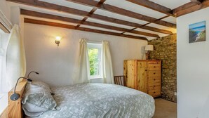 A bedroom with a bed, a dresser, a window with curtains, and a stone wall. - 1 Bed in Tremar (oc-w44759) (Tremar)