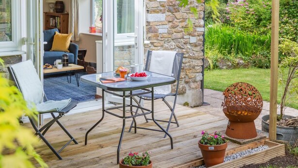 A patio with a table and chairs, a stone wall, and potted plants. - 1 Bed in Tremar (oc-w44759) (Tremar)