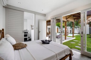A modern bedroom with a bed, a wardrobe, and a view of a pool and garden. - Villa Nakal in Seminyak (Seminyak)