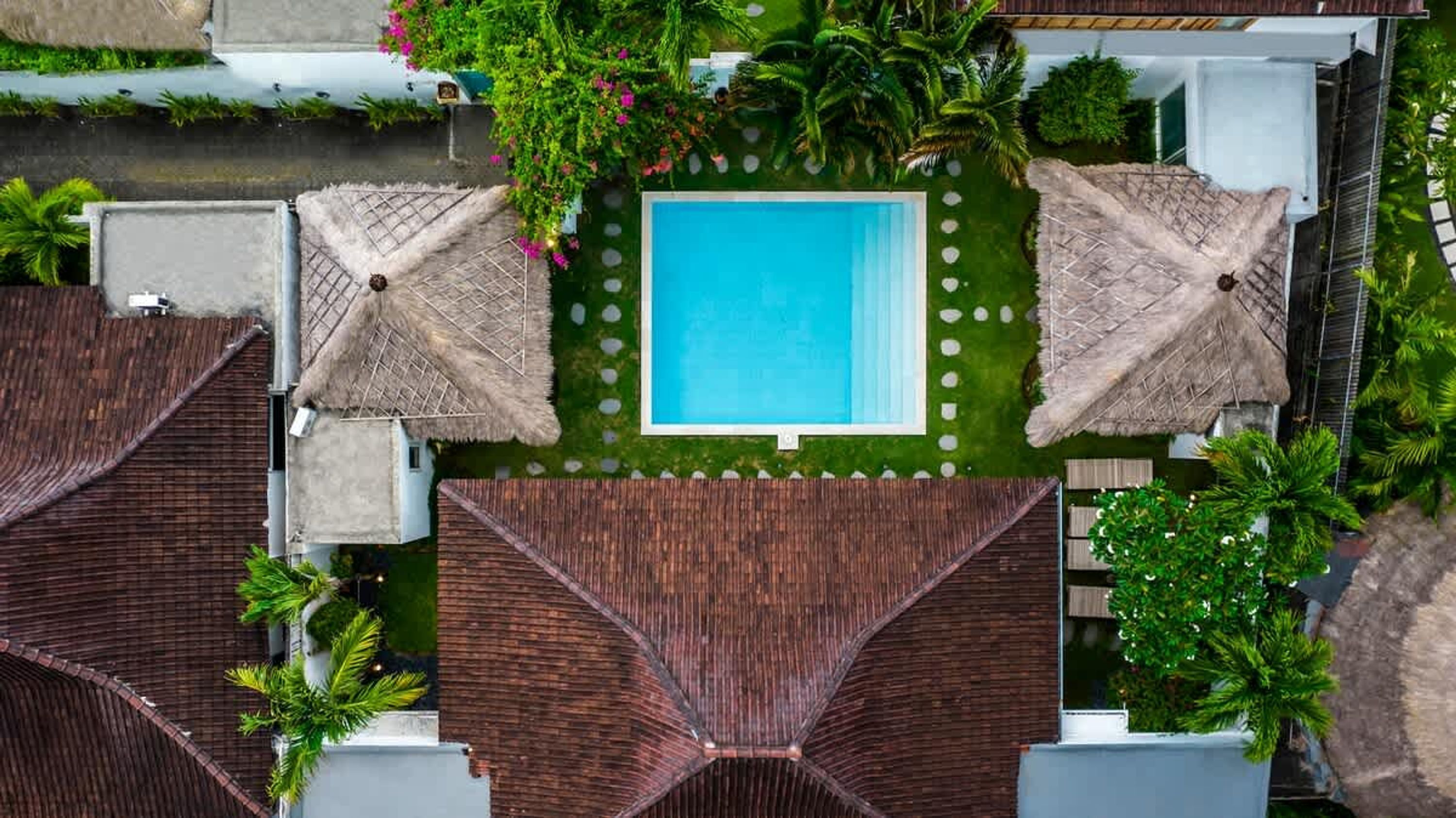 A rooftop pool surrounded by thatched umbrellas, palm trees, and a well-maintained lawn.