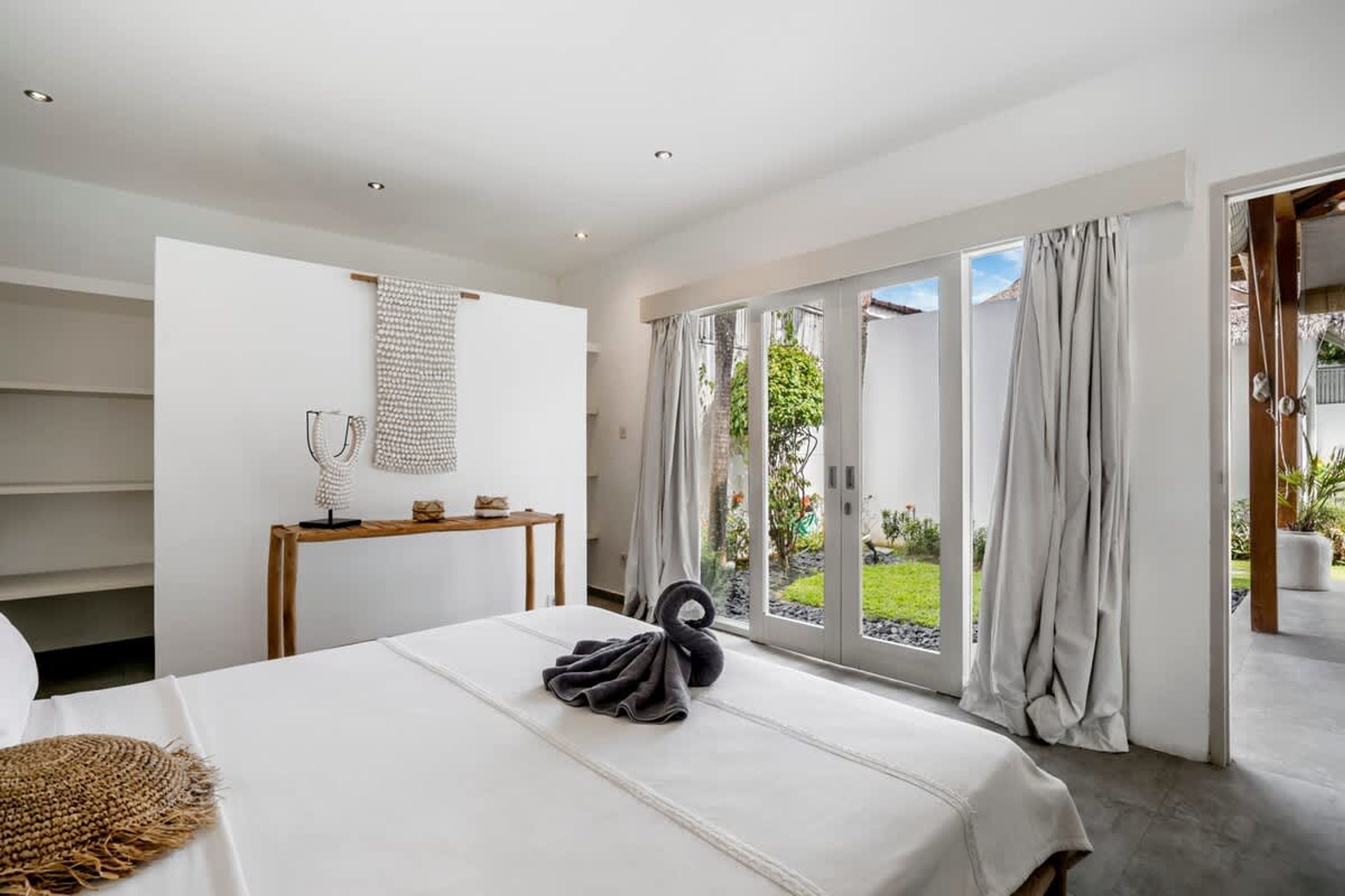 Ein modernes Hotelzimmer mit einem Bett, einem Nachttisch, einer kleinen Konsole und Blick ins Freie durch große Fenster.
