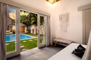 A bedroom with a sliding glass door leading to a pool, a bench, and a macrame wall hanging. - Villa Nakal in Seminyak (Seminyak)