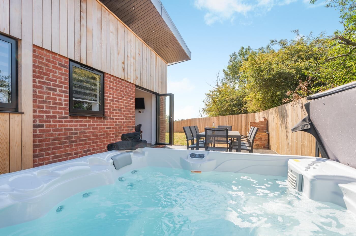 A hot tub in a backyard with a wooden deck, a brick wall, and a wooden fence.