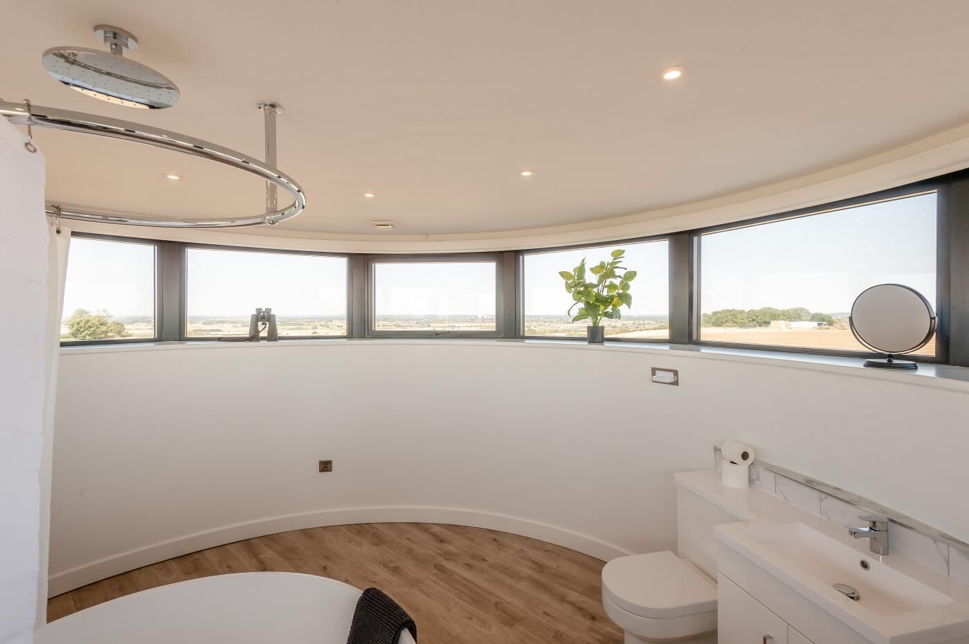 A modern bathroom with a bathtub, toilet, and sink. There are large windows offering a view of the landscape.
