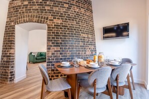 A dining area with a brick wall, a television mounted on the wall, and a table set for breakfast. - 4 Bed in Waddington (oc-w42854) (Waddington)