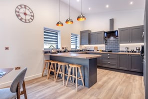 Una cocina moderna con una isla central, taburetes de bar, iluminación colgante y armarios grises.