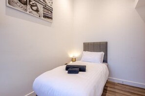 A neatly made bed with white linens and a grey headboard, a bedside lamp, and a framed picture on the wall. - 4 Bed in Waddington (oc-w42854) (Waddington)