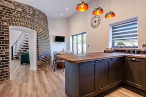 Cocina moderna con pared de ladrillo curva, suelo de madera e iluminación colgante.