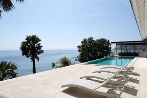 Ein Poolbereich mit Liegestühlen, freier Meerblick und einem modernen Gebäudebau.