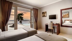 A hotel room with two beds, a desk, a chair, a TV, and a view of the ocean. - Villa Eden Roc in BANYUNING,  AMED,  ABANG, (BANYUNING,  AMED,  ABANG,)