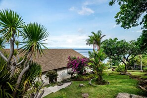 Ein Haus mit Ziegeldach, umgeben von einem gepflegten Garten mit verschiedenen Pflanzen und Blick auf den Ozean.