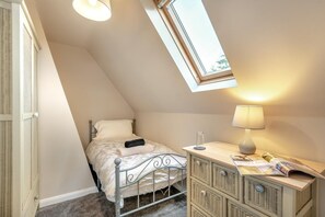 Ein Schlafzimmer mit schrägen Wänden, einem Bett, einem Nachttisch mit Lampe, einem Fenster und einem Kleiderschrank.
