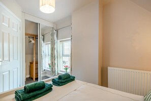 Ein Schlafzimmer mit einem Bett, einem Spiegel, einem Heizkörper und einem Fenster mit Vorhängen.