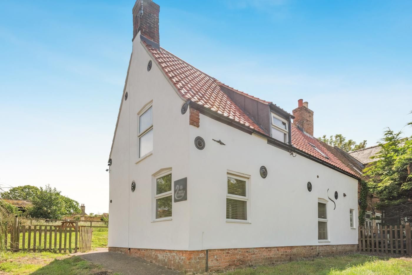 Et hvidt hus med rødt tegltag, en murstens skorsten og en lille have.