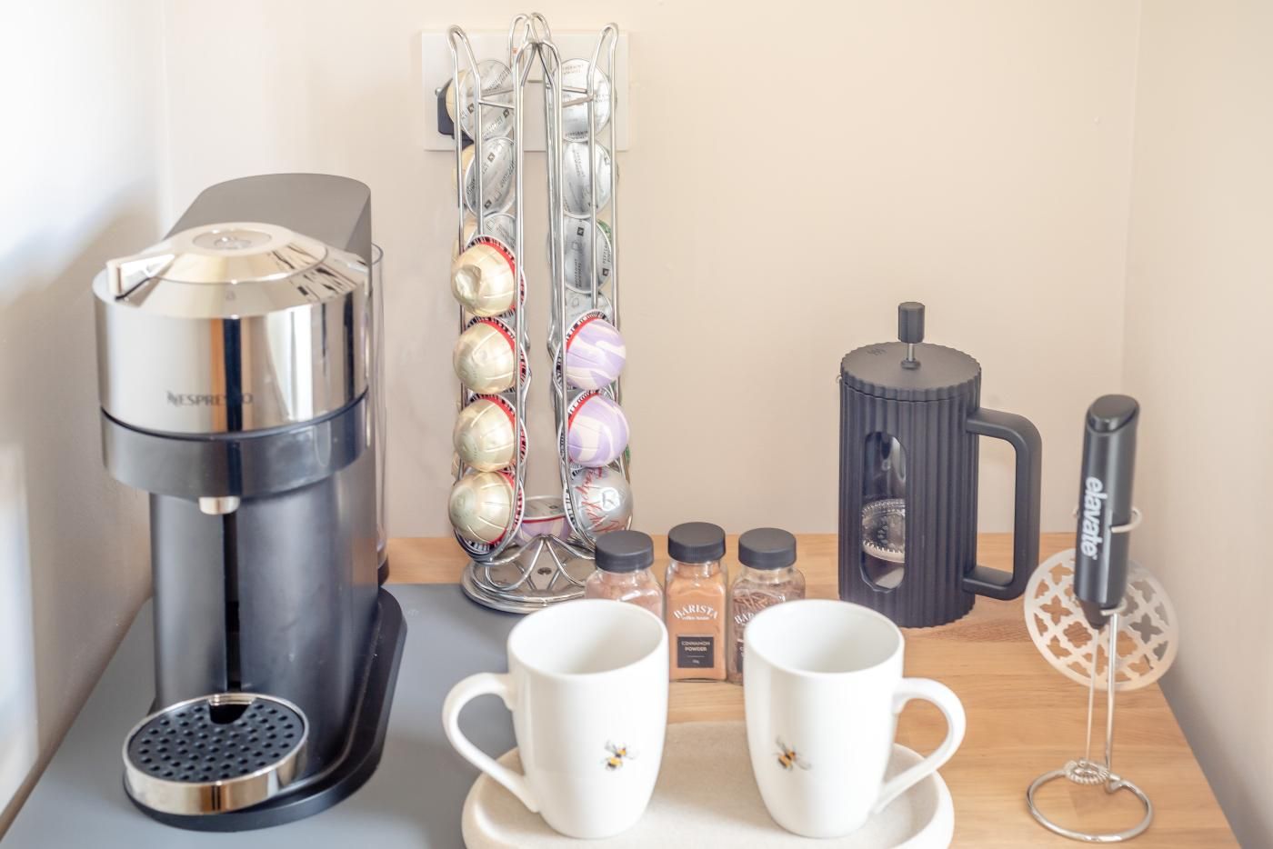 A coffee machine, a coffee grinder, a spice rack, and two cups on a table.