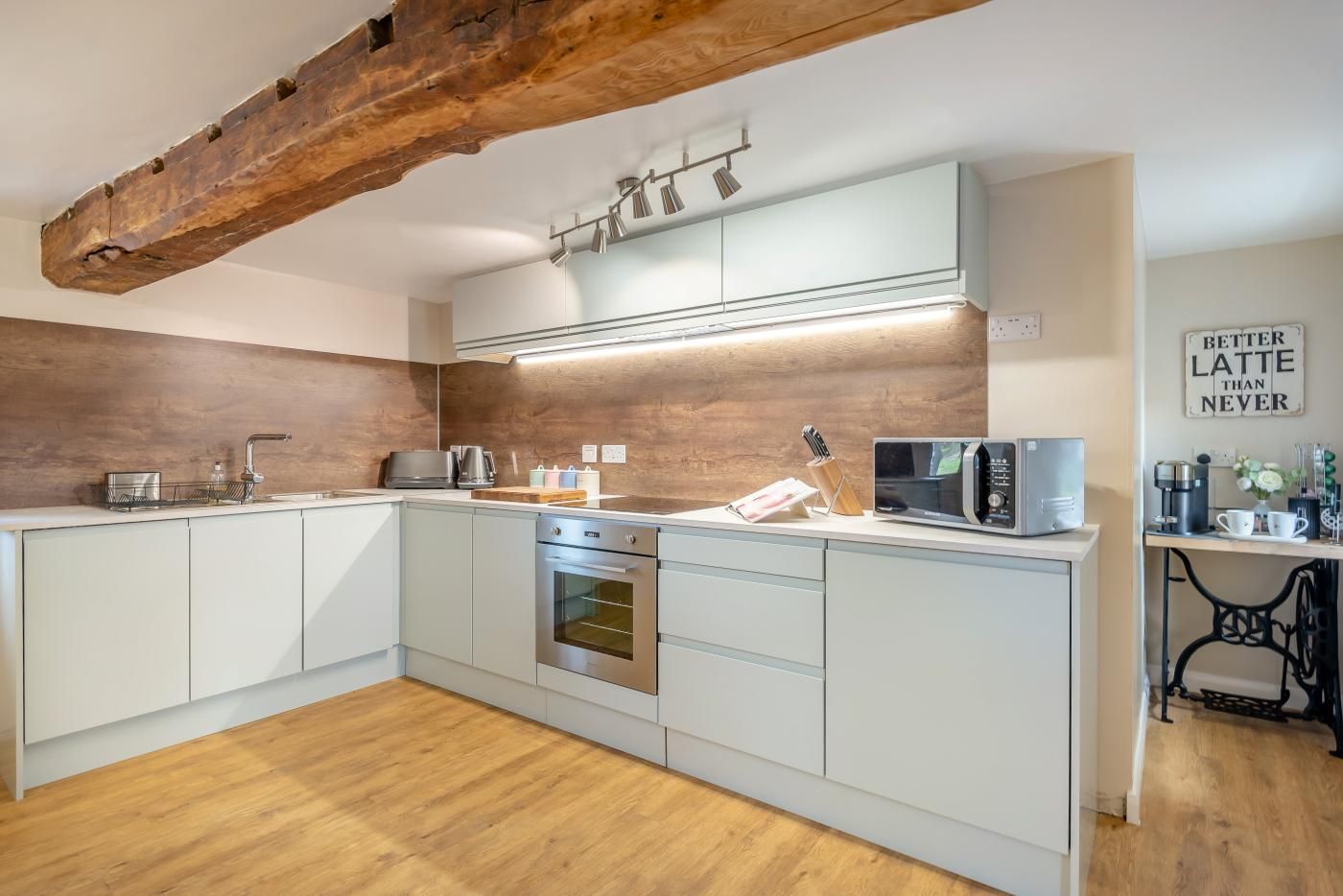 A modern kitchen with a central island, built-in oven, and a wooden ceiling beam.