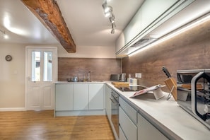 Eine moderne Küche mit Holzbalkendecke, weißen Schränken, einem eingebauten Backofen und einer Arbeitsplatte mit Messerblock und Wasserkocher.