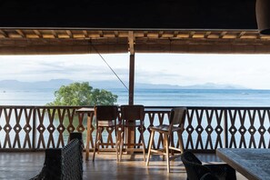 Um deque de madeira com vista para o mar e montanhas, com uma mesa e cadeiras.