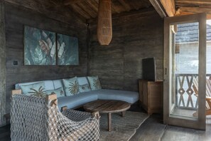 A wooden interior with a sofa, a hanging light fixture, and a view through a glass door. - Sunset Beachwood Villa (Nusa Lembongan)