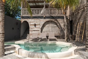Un área de piscina con una estructura de piedra, palmeras y sillas de descanso.