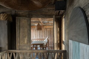 Um interior rústico de madeira, com teto de palha, um banco e um candeeiro pendente.