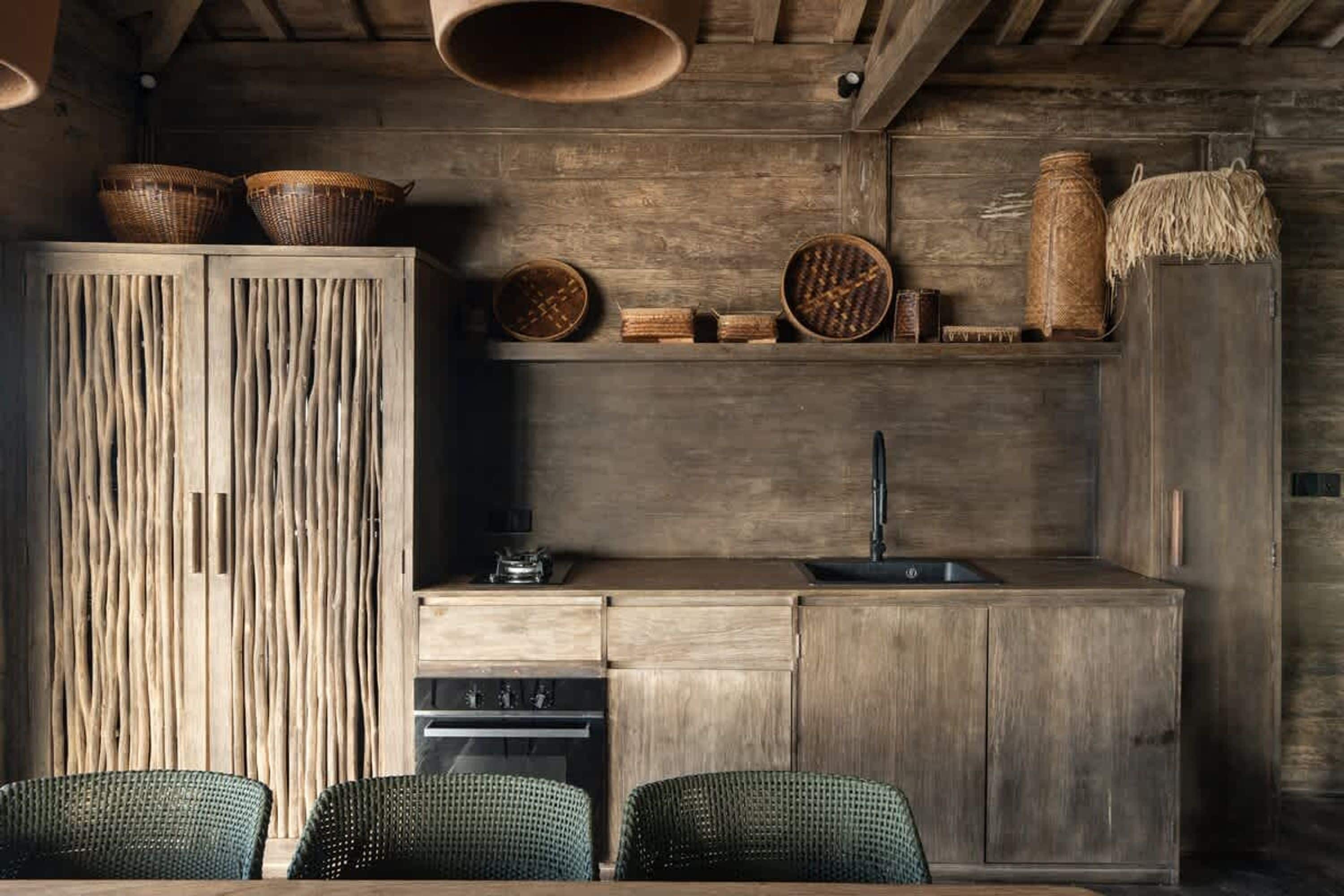 A rustic kitchen with wooden cabinets, a sink, and woven baskets on shelves.