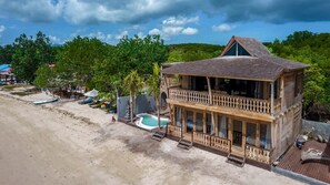 A two-story wooden building with a balcony, a swimming pool, and beach chairs. - Sunset Beachwood Villa (Nusa Lembongan)