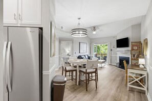 A modern kitchen with a built-in refrigerator, a dining area with a round table and chairs, a ceiling fan, and a fireplace. - Coastal Condo: Pet friendly/Pool/Mins to UNCW, Downtown & Wrightsville Beach (Wilmington)