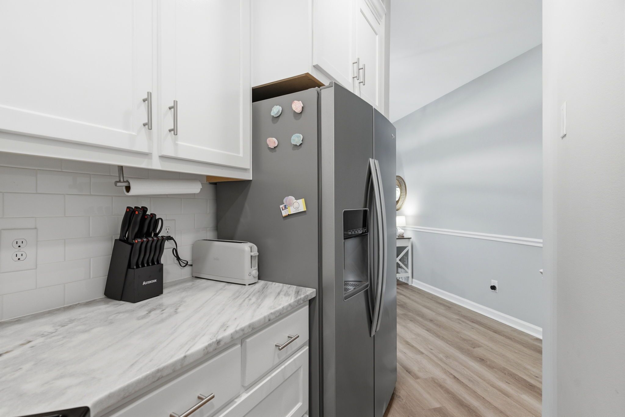 Una cocina moderna con armarios blancos, encimera de mármol, refrigerador de acero inoxidable y un tostador.