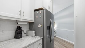 A modern kitchen with white cabinets, a marble countertop, a stainless steel refrigerator, and a toaster. - Coastal Condo: Pet friendly/Pool/Mins to UNCW, Downtown & Wrightsville Beach (Wilmington)
