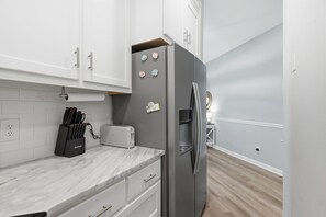 A modern kitchen with white cabinets, a marble countertop, a stainless steel refrigerator, and a toaster. - Coastal Condo: Pet friendly/Pool/Mins to UNCW, Downtown & Wrightsville Beach (Wilmington)