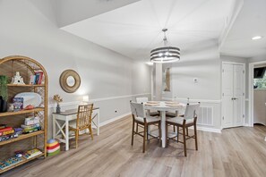 A dining area with a round table, chairs, a bookshelf, and a hanging light fixture. - Coastal Condo: Pet friendly/Pool/Mins to UNCW, Downtown & Wrightsville Beach (Wilmington)