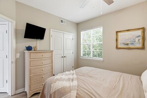 A bedroom with a bed, a television mounted on the wall, a dresser, a window with blinds, and a framed picture on the wall. - Coastal Condo: Pet friendly/Pool/Mins to UNCW, Downtown & Wrightsville Beach (Wilmington)
