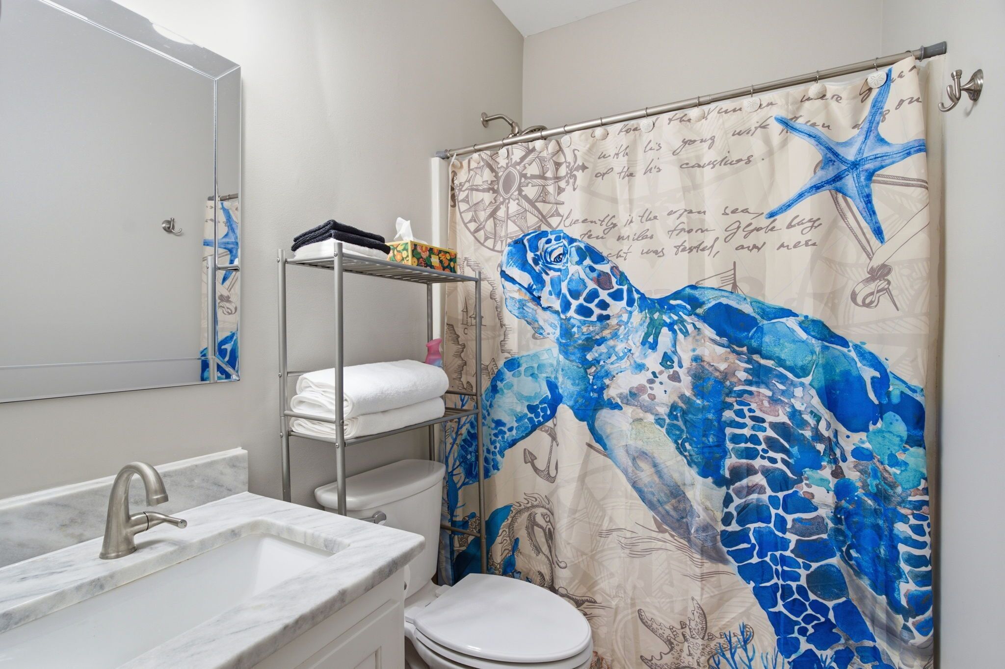 Baño con cortina de ducha decorada con un diseño de tortuga marina, un lavamanos blanco y un inodoro.