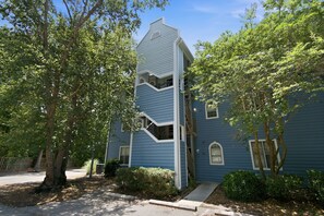 A blue two-story house with a unique architectural design, including a central staircase and a small balcony. - Coastal Condo: Pet friendly/Pool/Mins to UNCW, Downtown & Wrightsville Beach (Wilmington)