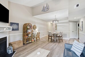 A living room with a fireplace, a dining area with a chandelier, and a bookshelf. - Coastal Condo: Pet friendly/Pool/Mins to UNCW, Downtown & Wrightsville Beach (Wilmington)