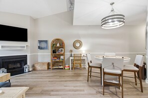 A living room with a fireplace, a television, a dining area with chairs, and a chandelier. - Coastal Condo: Pet friendly/Pool/Mins to UNCW, Downtown & Wrightsville Beach (Wilmington)