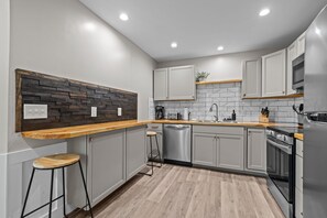 Eine moderne Küche mit grauen Schränken, einer Holz Arbeitsplatte, einem Geschirrspüler und einem Backofen.