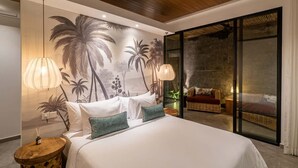 Una camera da letto con un letto, due lampade ai comodini, un affresco, una sedia in vimini e una porta scorrevole in vetro che dà su un balcone.