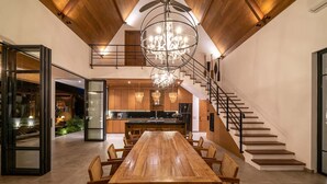Un'ampia sala da pranzo con un lungo tavolo di legno e sedie, un lampadario e una scala che conduce a un piano superiore.