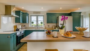 A modern kitchen with teal cabinets, a central island, and a view of greenery outside. - 2 Bed in Docking (oc-t44851) (Docking)