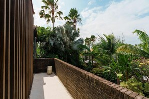 A balcony with a brick wall, surrounded by various tropical plants and palm trees. - Villa Pakuk in Kecamatan Kuta Utara (Kecamatan Kuta Utara)